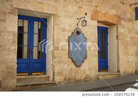 Building facade, blue doors, lantern and wooden notice board on wall outdoors Building facade, blue doors, lantern and wooden notice board on wall outdoors 108570230