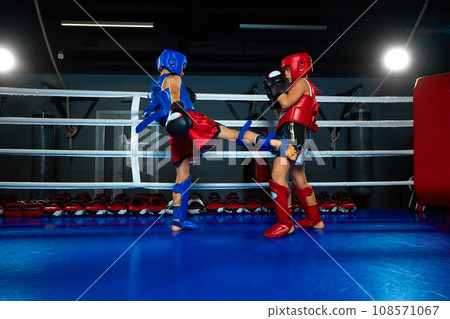 Healthy boy, kickboxer in uniform training kickboxing with sparring partner in ring at sport gym. Pupil sportsmen. 108571067