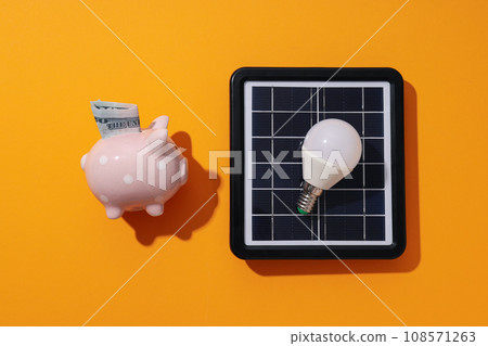 Solar panel, light bulb and piggy bank on orange background, top view Solar panel, light bulb and piggy bank on orange background, top view 108571263