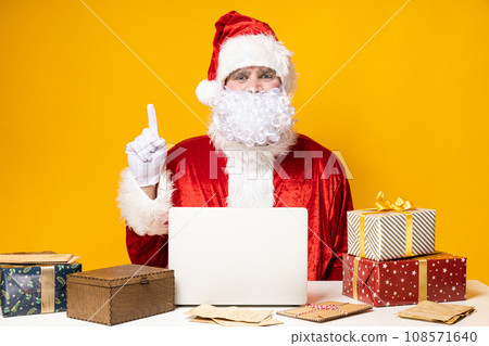Santa Claus, at the table with a laptop, on a yellow background. Santa Claus, at the table with a laptop, on a yellow background. 108571640