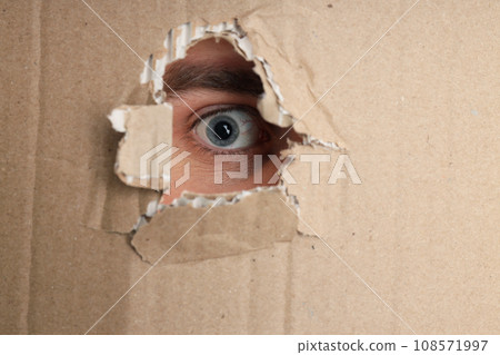 Human eyes in the hole of a cardboard box 108571997