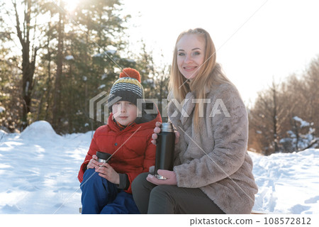 Portrait of mother and son snowy in forest drinking hot tea from thermos. Winter holidays. Portrait of mother and son snowy in forest drinking hot tea from thermos. Winter holidays. 108572812