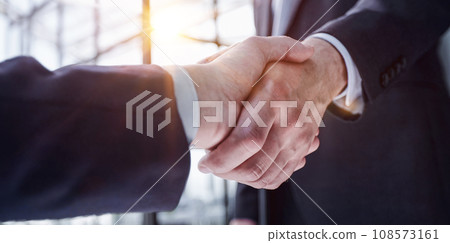 executives shaking hands in front of their manager and a colleague 108573161