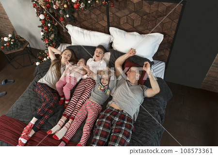 Christmas decorations. Young mother father and kids together. Happy young family with three children in bed in pajamas. Top view. 108573361