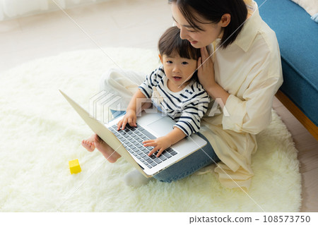 A mother looking at a computer while holding her child 108573750