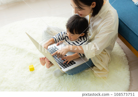 A mother looking at a computer while holding her child 108573751