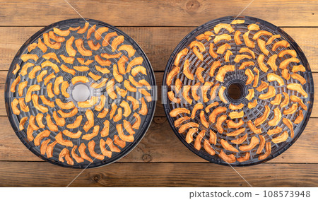 Two sections of fruit and vegetable dryer with dried apples on a wooden background. 108573948