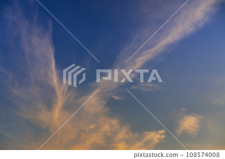 Evening cloudscape. White high-level cirrus clouds with orange tint against a blue sky. Landscape orientation. Evening cloudscape. White high-level cirrus clouds with orange tint against a blue sky. Landscape orientation. 108574008