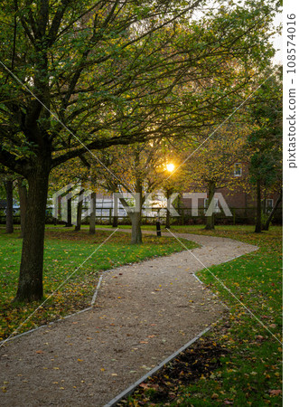 Autumn (fall) scene in England with a footpath leading through a park with trees. The setting sun is visible through the leaves. Autumn (fall) scene in England with a footpath leading through a park with trees. The setting sun is visible through the leaves. 108574016