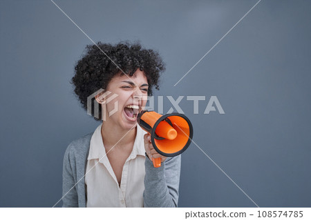 a girl on a gray background holds a loudspeaker in her hand. screams 108574785
