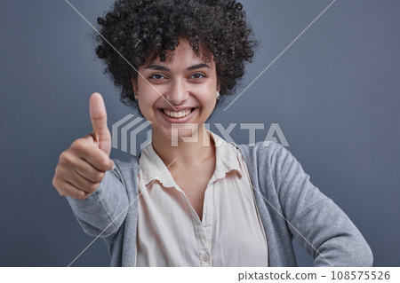 girl on a gray background smiling and showing a raised thumb girl on a gray background smiling and showing a raised thumb 108575526