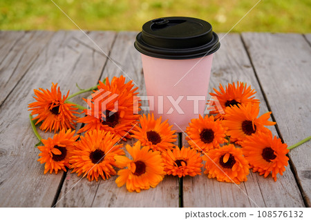 Calendula flowers are lying on an old wooden table near a glass of coffee or tea. Phytotherapy. Calendula flowers are lying on an old wooden table near a glass of coffee or tea. Phytotherapy. 108576132