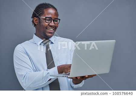 young african american man on gray background holding laptop showing victory sign 108576640