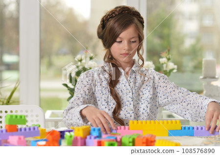Portrait of cute girl playing with colorful plastic blocks in room 108576890