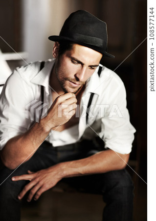 Man, hipster and thinking about fashion, ideas or choice of clothes in dark background. Clothing, decision and creative person or model sitting and planning outfit with vintage hat and retro style Man, hipster and thinking about fashion, ideas or choice of clothes in dark background. Clothing, decision and creative person or model sitting and planning outfit with vintage hat and retro style 108577144