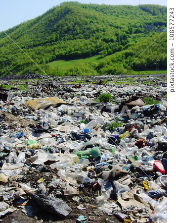 Pollution, waste or refuse with litter in nature against a green mountain as a danger of climate change. Global warming, garbage and trash, toxic to the environment on an illegal dump or landfill 108577243