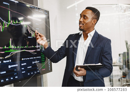 African man in a black suit. Big TV screen. Guy shows presentation. African man in a black suit. Big TV screen. Guy shows presentation. 108577283