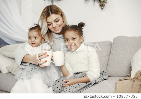 People reparing for Christmas. Mother playing with her daughters. Family is resting in a festive room. Child in a sweater sweater. People reparing for Christmas. Mother playing with her daughters. Family is resting in a festive room. Child in a sweater sweater. 108577355