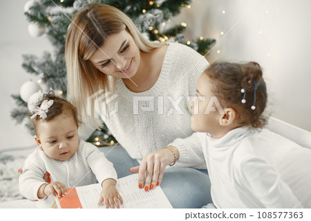 People reparing for Christmas. Mother playing with her daughters. Family is resting in a festive room. Child in a sweater sweater. 108577363