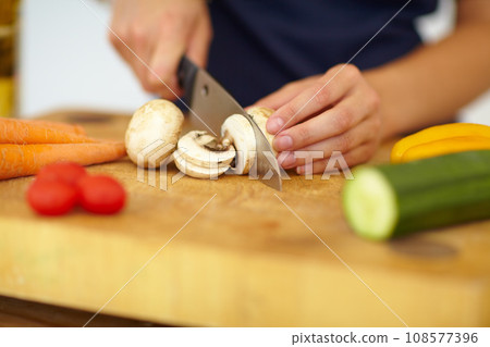 Chef hands, knife and vegetables on chopping board, cooking and preparation at home. Closeup of woman cutting mushrooms in kitchen, organic salad and food for healthy vegan diet, nutrition and dinner 108577396
