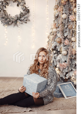 Elegant lady near Christmass tree. Woman in a room. Famale in a silver dress. 108577437