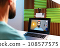 a young man takes pictures of himself on the phone and displays the video on the laptop screen 108577575