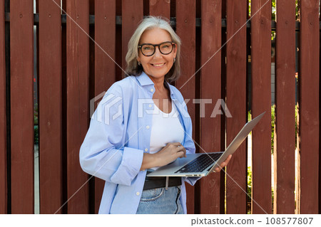 well-groomed middle-aged woman with a bob haircut works freely using a laptop on the street well-groomed middle-aged woman with a bob haircut works freely using a laptop on the street 108577807