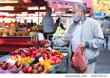 Man in face mask choosing tomatoes in greengrocery Man in face mask choosing tomatoes in greengrocery 108578331