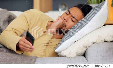 Man, phone and cough on sofa in home living room, texting or communication with email notification. Guy, smartphone and sick with research for health, medicine or watch video on social media in house 108578753