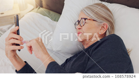 Phone, relax and elderly woman in bed networking on social media, mobile app or internet. Technology, rest and senior female person in retirement scroll on website with cellphone in bedroom at home. 108578924