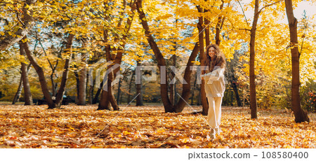 Smiling running woman plays and jumping dancing in the autumn forest with the yellow leaves at sunset. Copy space. 108580400