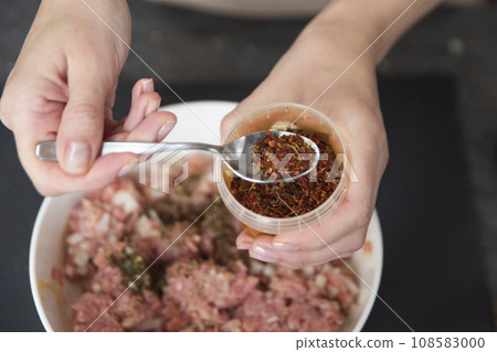 A woman's hand sprinkles ground paprika on a raw meat close-up. Freshly ground paprika is used as a raw meat dressing. 108583000