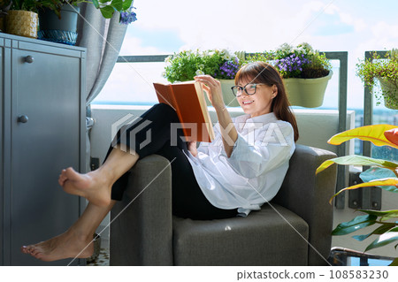 Middle-aged relaxed happy woman reading book, sitting at home 108583230