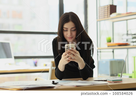 Satisfied woman sends messages to boyfriend from office Satisfied woman sends messages to boyfriend from office 108584026