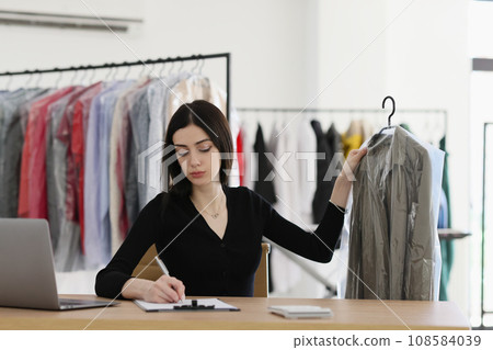 Woman makes notes on clipboard holding coat under film 108584039