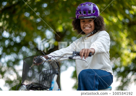 Smiling dark-skinned girl on a bike in a park Smiling dark-skinned girl on a bike in a park 108584192