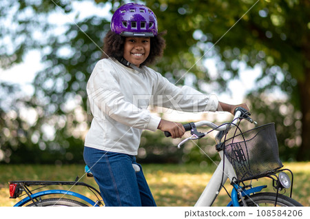 Smiling dark-skinned girl on a bike in a park Smiling dark-skinned girl on a bike in a park 108584206