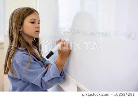 Cute fair-haired schoolgirl writing on the board and looking concentrated 108584291