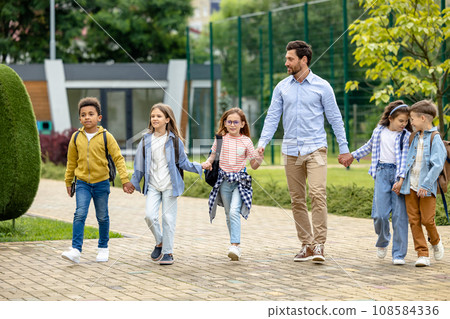 Male teacher and his pupils at the school yard feeling happy Male teacher and his pupils at the school yard feeling happy 108584336