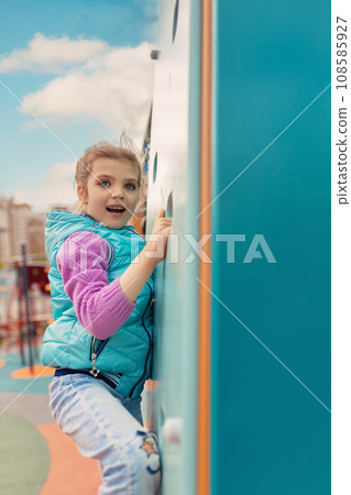 happy smiling cheerful girl 6 years old holding on climbing wall, children's sport at playground happy smiling cheerful girl 6 years old holding on climbing wall, children's sport at playground 108585927