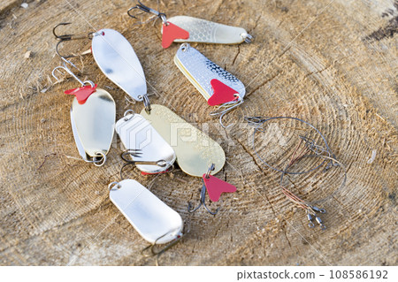artificial metal baits on a wooden background. Homemade fishing gear. baits for catching large predatory fish. Items are made of different metal alloys of different colors and shapes 108586192