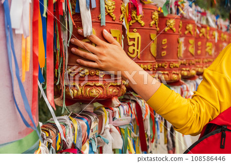 Person pilgrim female hand touching turning spinning Buddhist prayer wheel at Buddhist monastery. Prayer wheels in Buddhist stupa temple. Buddhism religion concept Person pilgrim female hand touching turning spinning Buddhist prayer wheel at Buddhist monastery. Prayer wheels in Buddhist stupa temple. Buddhism religion concept 108586446