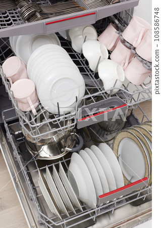 Open built-in dishwasher machine with clean cutlery, dishes, plates in white modern kitchen. top view Open built-in dishwasher machine with clean cutlery, dishes, plates in white modern kitchen. top view 108586748