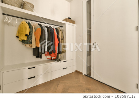 a closet with clothes hanging on the wall and wooden flooring in front of white cabinetd cupboards filled with colorful sweaters a closet with clothes hanging on the wall and wooden flooring in front of white cabinetd cupboards filled with colorful sweaters 108587112