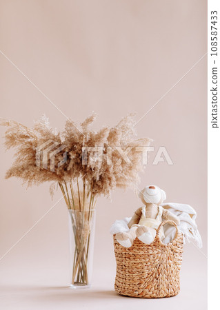 Interior of house of Natural accessories for home decor - dried plants in glass vase, wicker basket with teddy rabbit and plaid. Scandinavian cozy decor. copy space Interior of house of Natural accessories for home decor - dried plants in glass vase, wicker basket with teddy rabbit and plaid. Scandinavian cozy decor. copy space 108587433