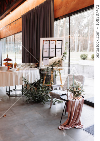 easel with wooden Stylish Board list seating plan for wedding reception. Vintage luxury wedding. table with fruit and champagne for guests easel with wooden Stylish Board list seating plan for wedding reception. Vintage luxury wedding. table with fruit and champagne for guests 108587472