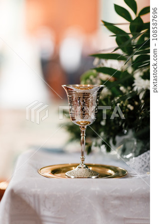 golden chalice with drawings on it for drinking wine for communion on the golden plate in church. Greens on background. copy space. selective focus 108587696