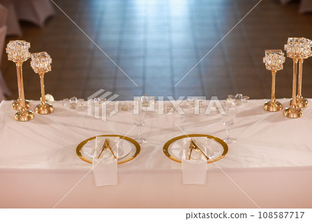 table decoration with pink tablecloth, crystal candlesticks with candles and white pink flowers in restaurant . stylish wedding day. setting table with gold plate, fork and knife 108587717
