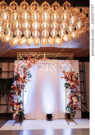 Beautiful wedding gold metal arch, wall, photo zone, area decorated with bright flowers and greens in hall for wedding ceremony. Festive decor in banquet area at party. Decorations in luxury ceremony Beautiful wedding gold metal arch, wall, photo zone, area decorated with bright flowers and greens in hall for wedding ceremony. Festive decor in banquet area at party. Decorations in luxury ceremony 108587797