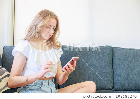 一位白人婦女坐在沙發上操作智慧型手機（思考） 108589276